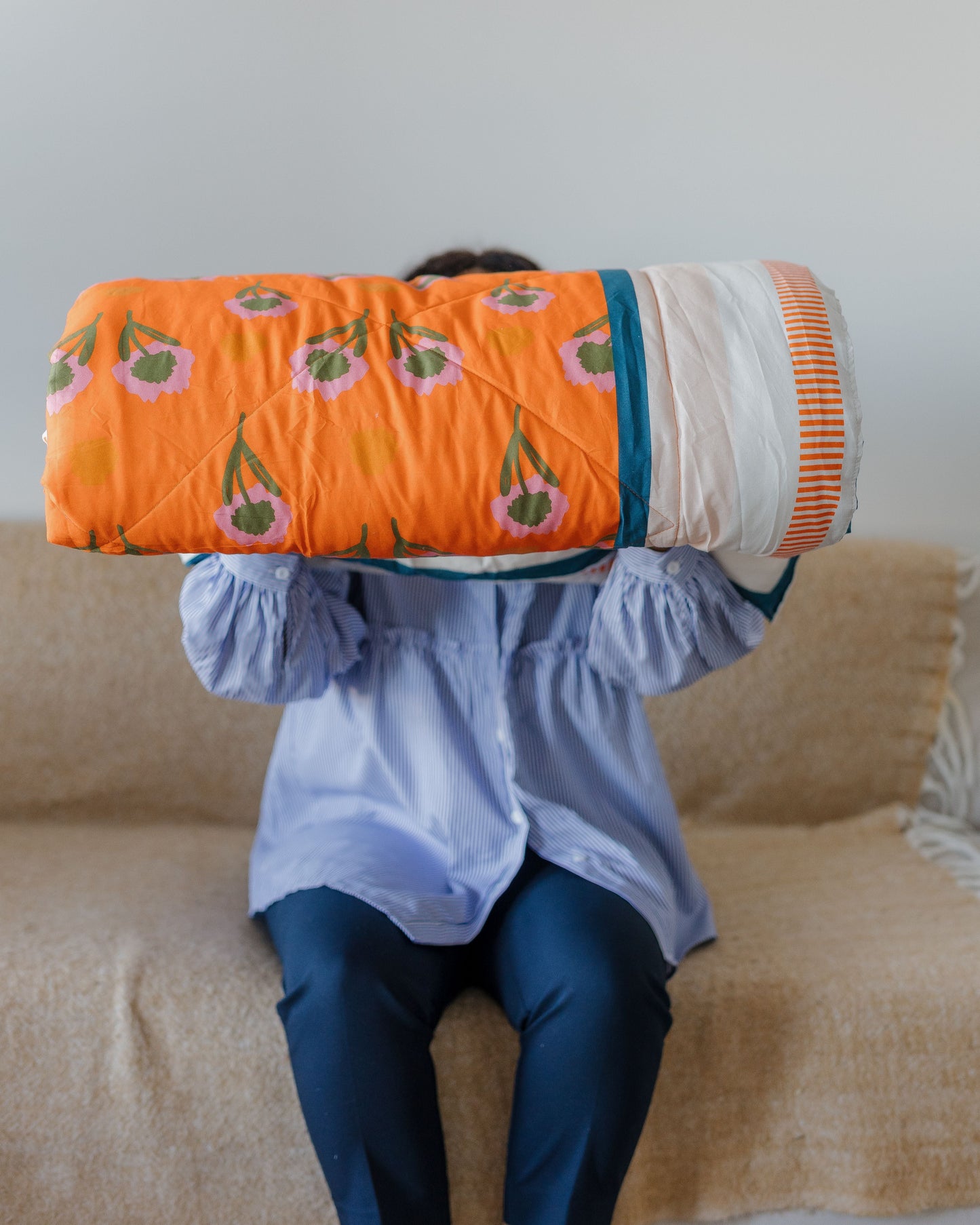Person holding a colorful quilt with a pattern of green leaves and orange flowers on a beige couch.
