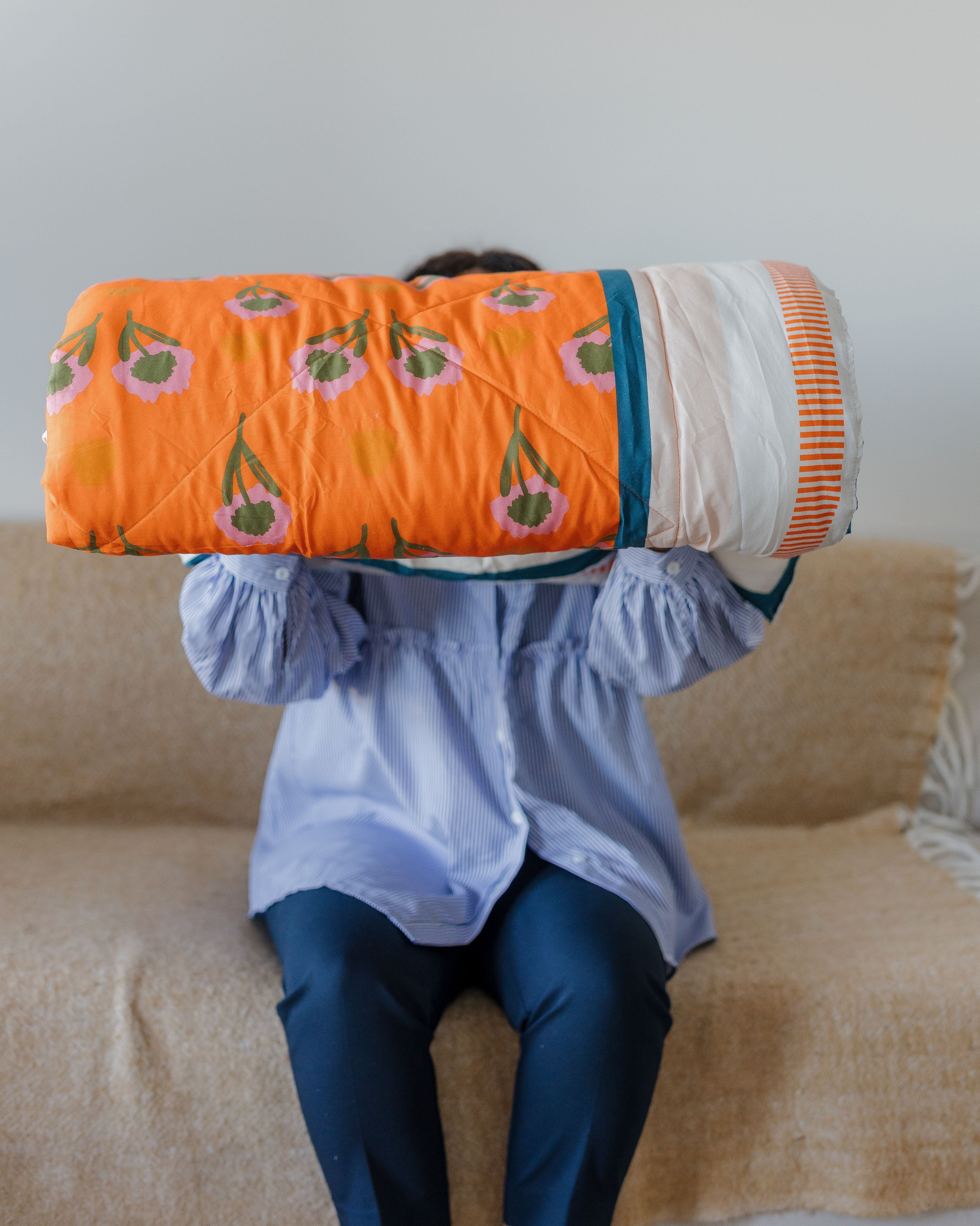 Person holding a colorful quilt with a pattern of green leaves and orange flowers on a beige couch.