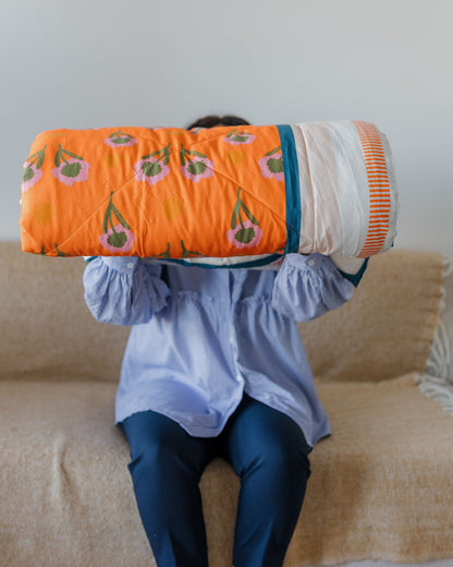 Person holding a colorful quilt with a pattern of green leaves and orange flowers on a beige couch.