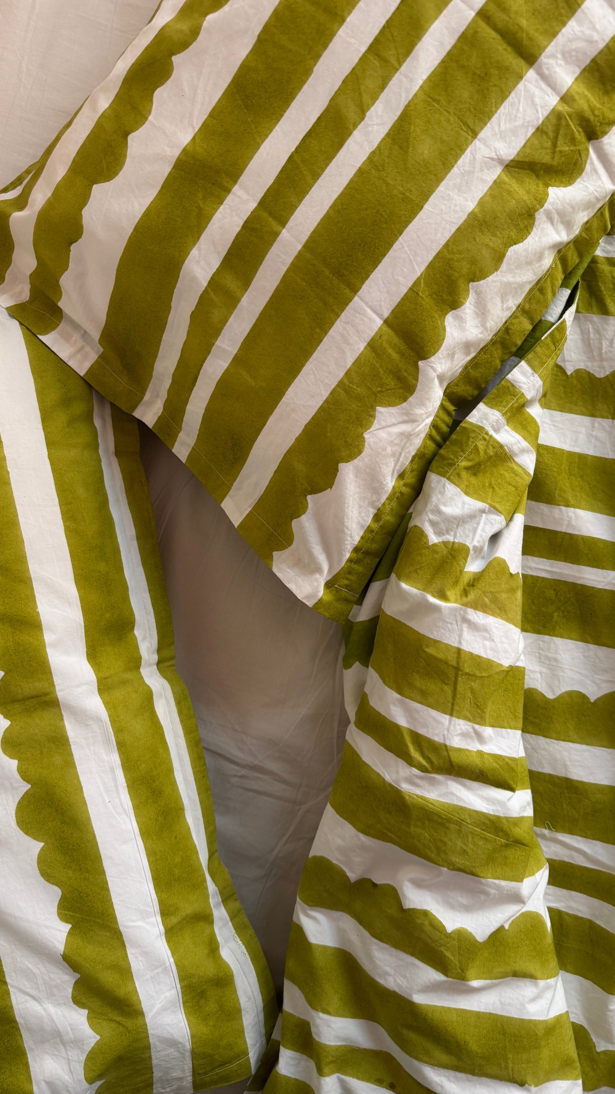 Close-up of striped bedding with olive green and white vertical stripes and scalloped edges, draped over a bed.