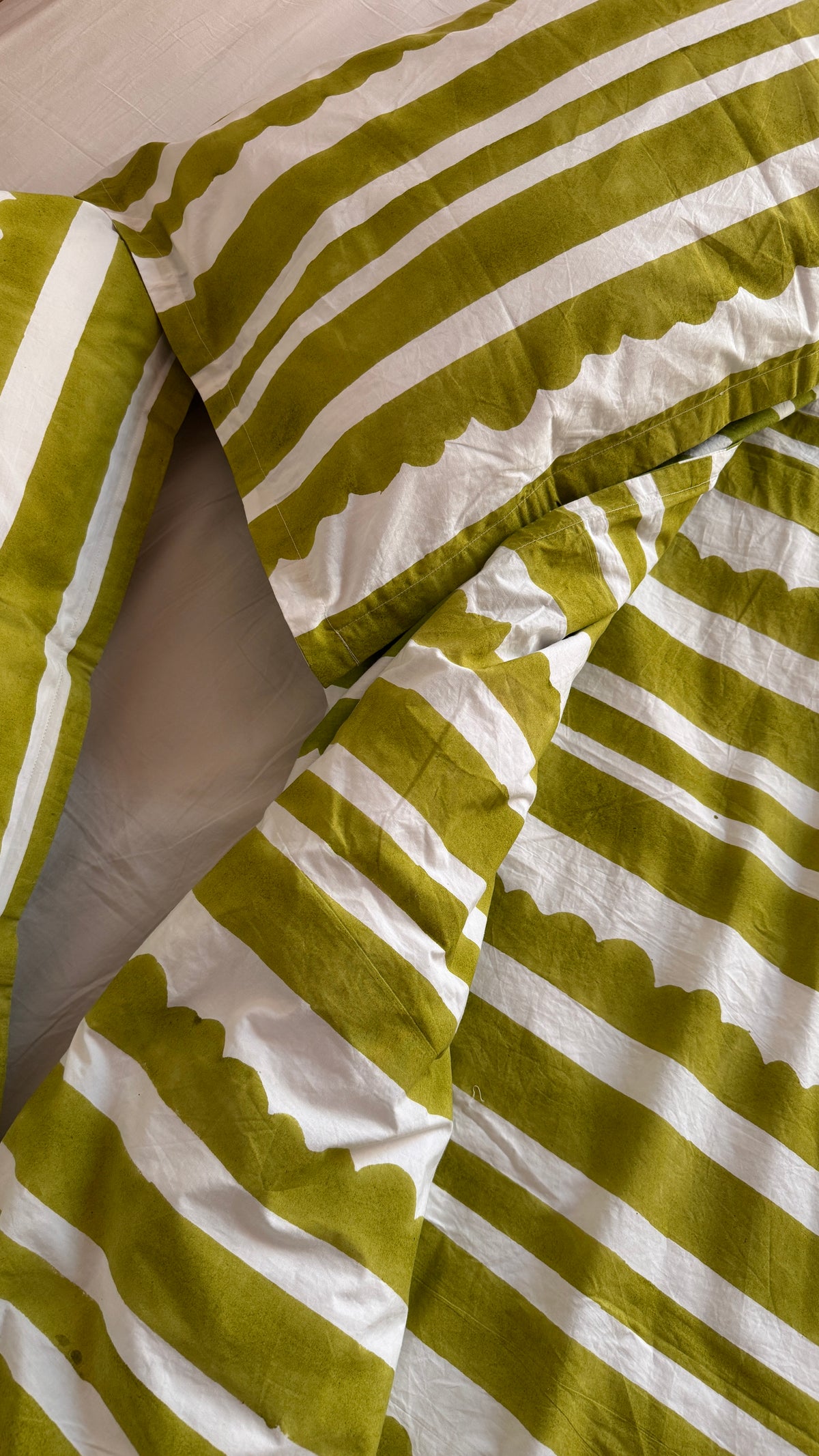 Close-up of a striped bedding set with olive green and white fabric featuring a scalloped edge pattern.