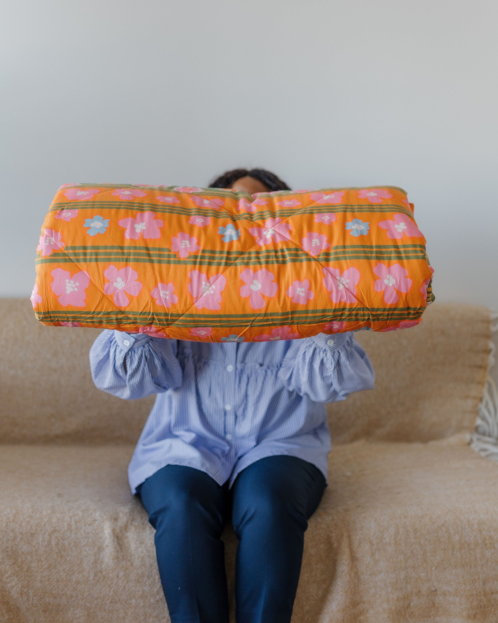 Person sitting on a couch holding an orange floral-patterned quilt blanket over their head.