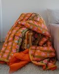 Floral-patterned orange blanket draped over a wooden chair against a white wall.