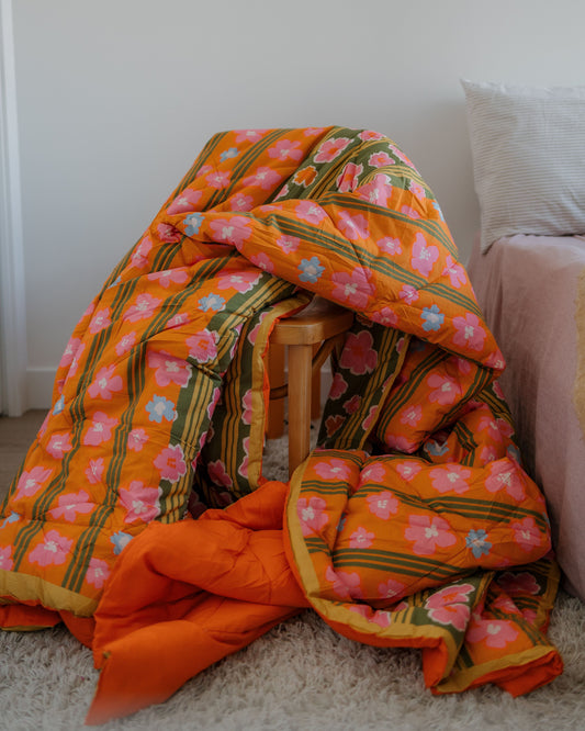 Floral-patterned orange blanket draped over a wooden chair against a white wall.