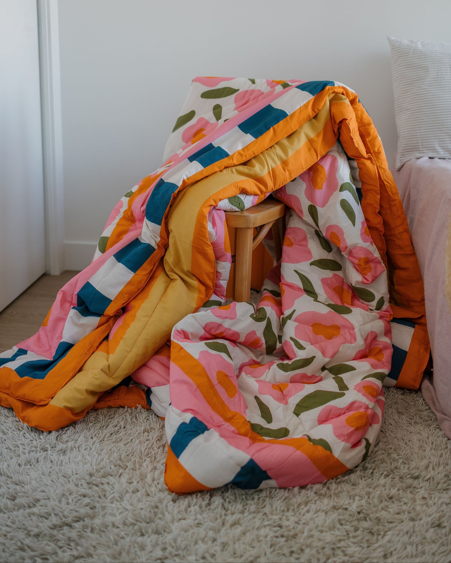 Colorful floral-patterned blanket draped over a chair and floor against a white wall.
