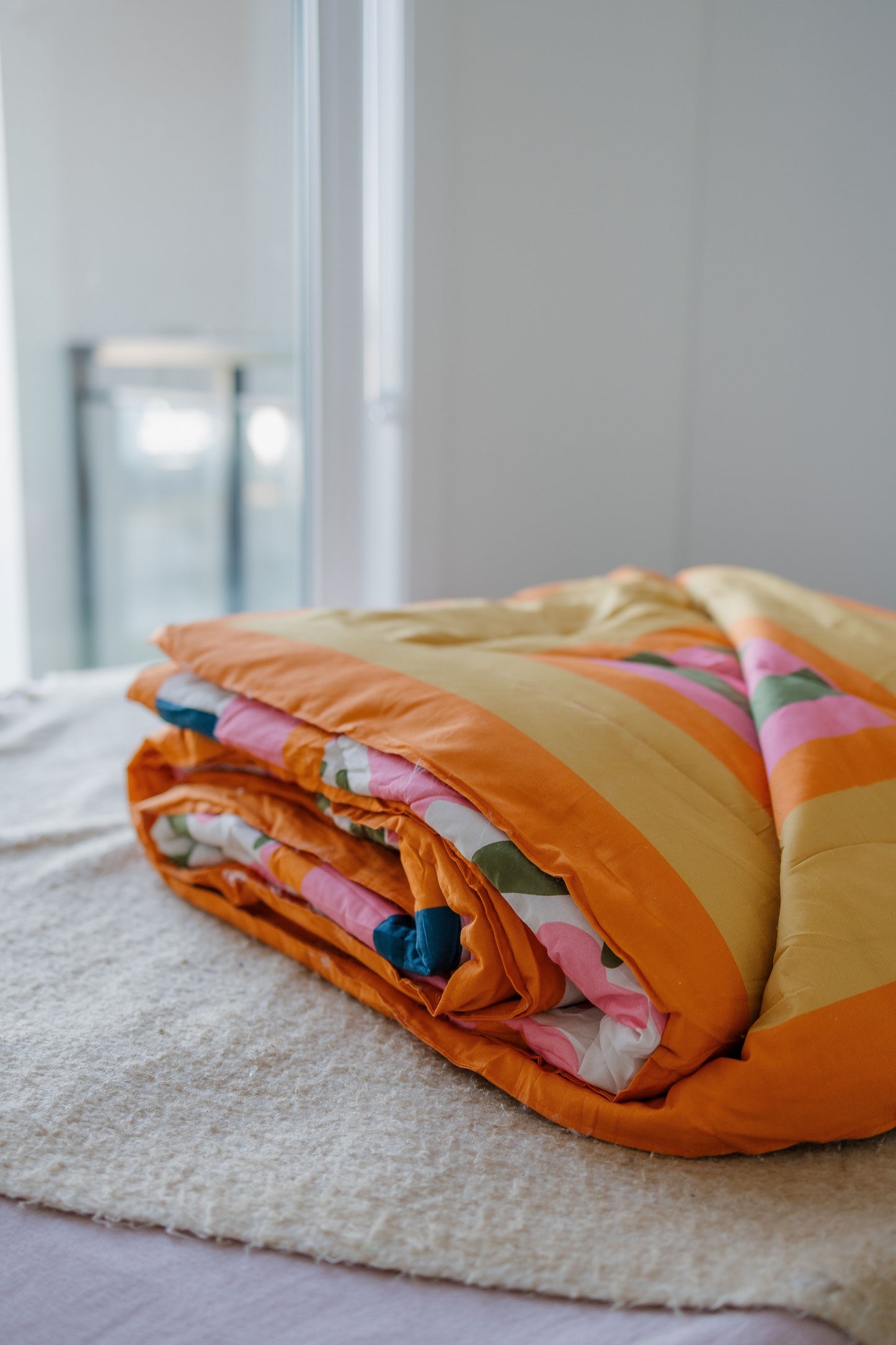 Folded colorful quilt on a bed with a neutral background