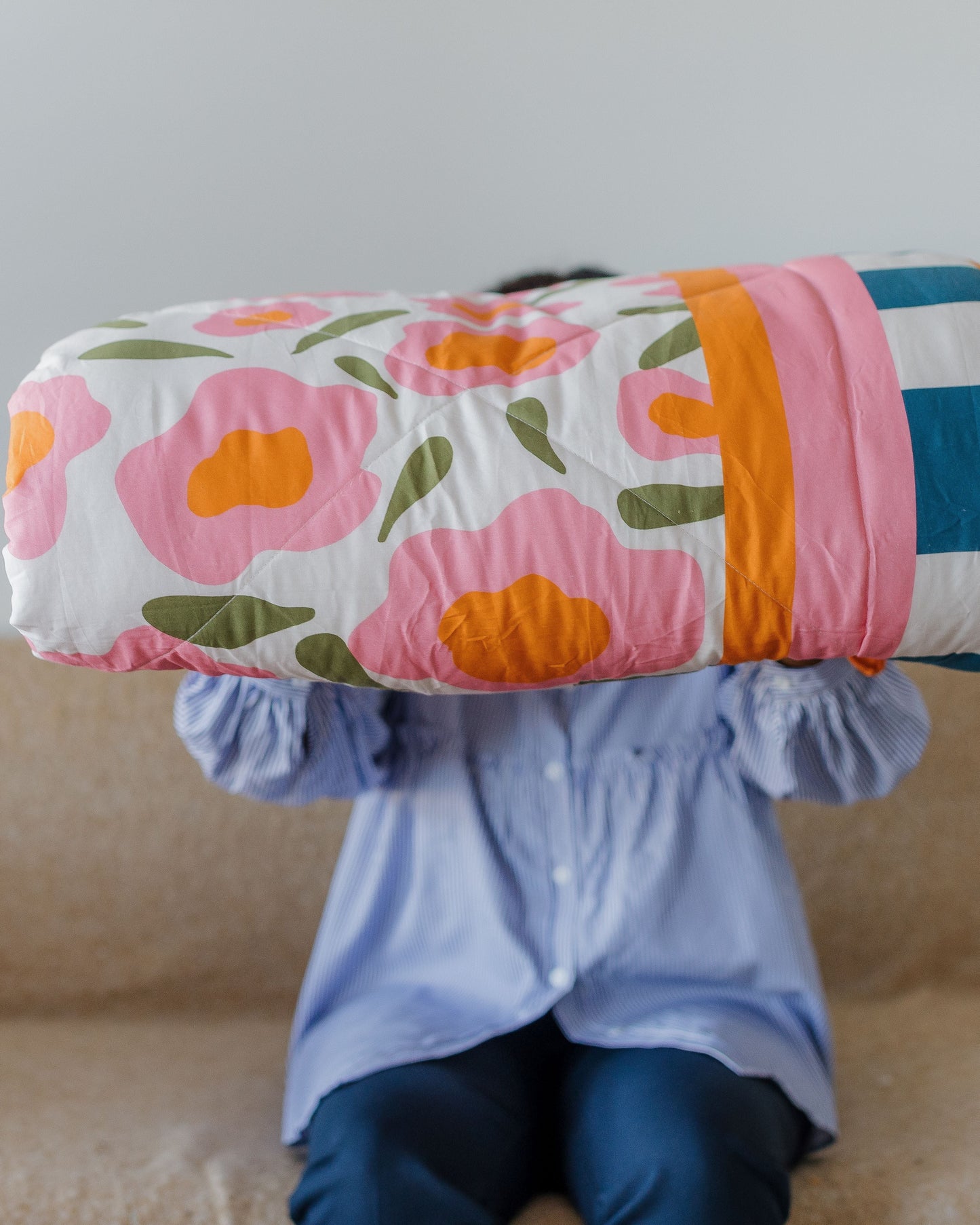 Person holding a colorful floral-patterned blanket over their head on a beige couch.