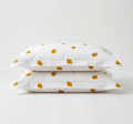 Two white pillowcases stacked on top of each other, featuring a scattered mustard yellow abstract polka dot pattern, set against a clean white studio background.
