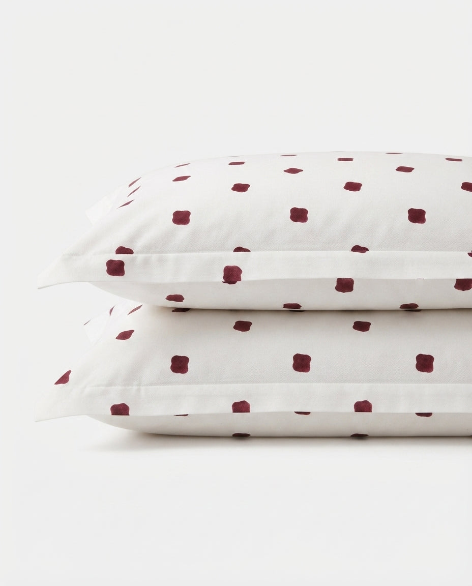 Two stacked white pillowcases with a small dark red square dot pattern, photographed on a clean white background.