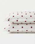 Two stacked white pillowcases with a small dark red square dot pattern, photographed on a clean white background.