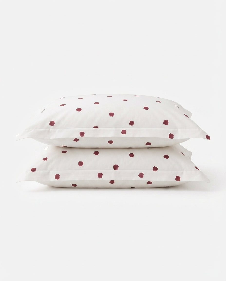 Two white pillowcases stacked on a light gray background, featuring a small dark red polka dot pattern.